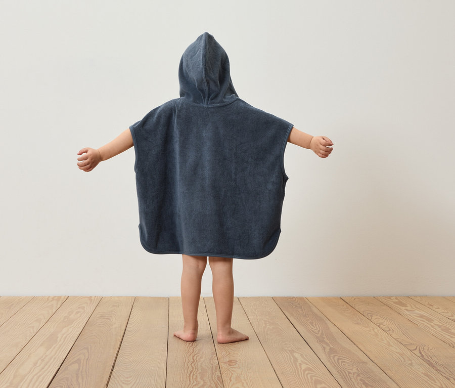 Un enfant, vu de dos, porte un poncho à capuche bleu marine et a les bras écartés.