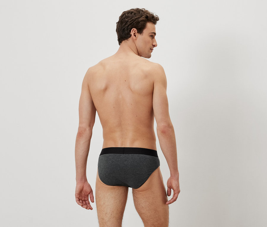 Un homme dos à la caméra porte un slip gris.