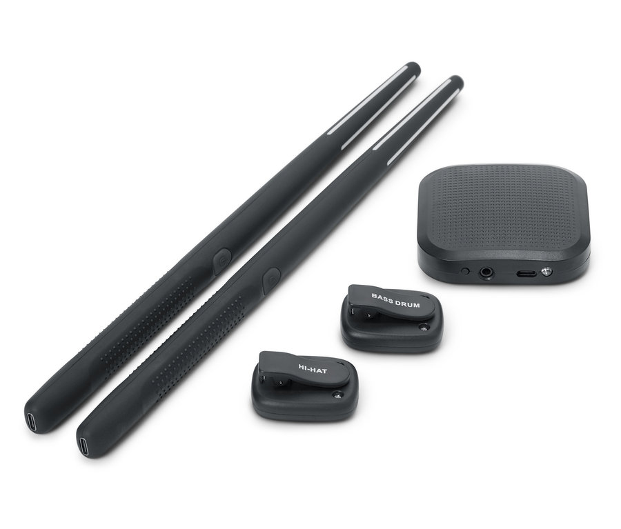 Deux baguettes de batterie noires sont placées l'une à côté de l'autre. Une boîte de son noire et deux petits pads de batterie noirs, l'un avec l'inscription BASS DRUM et l'autre avec l'inscription HI-HAT, sont également présents.