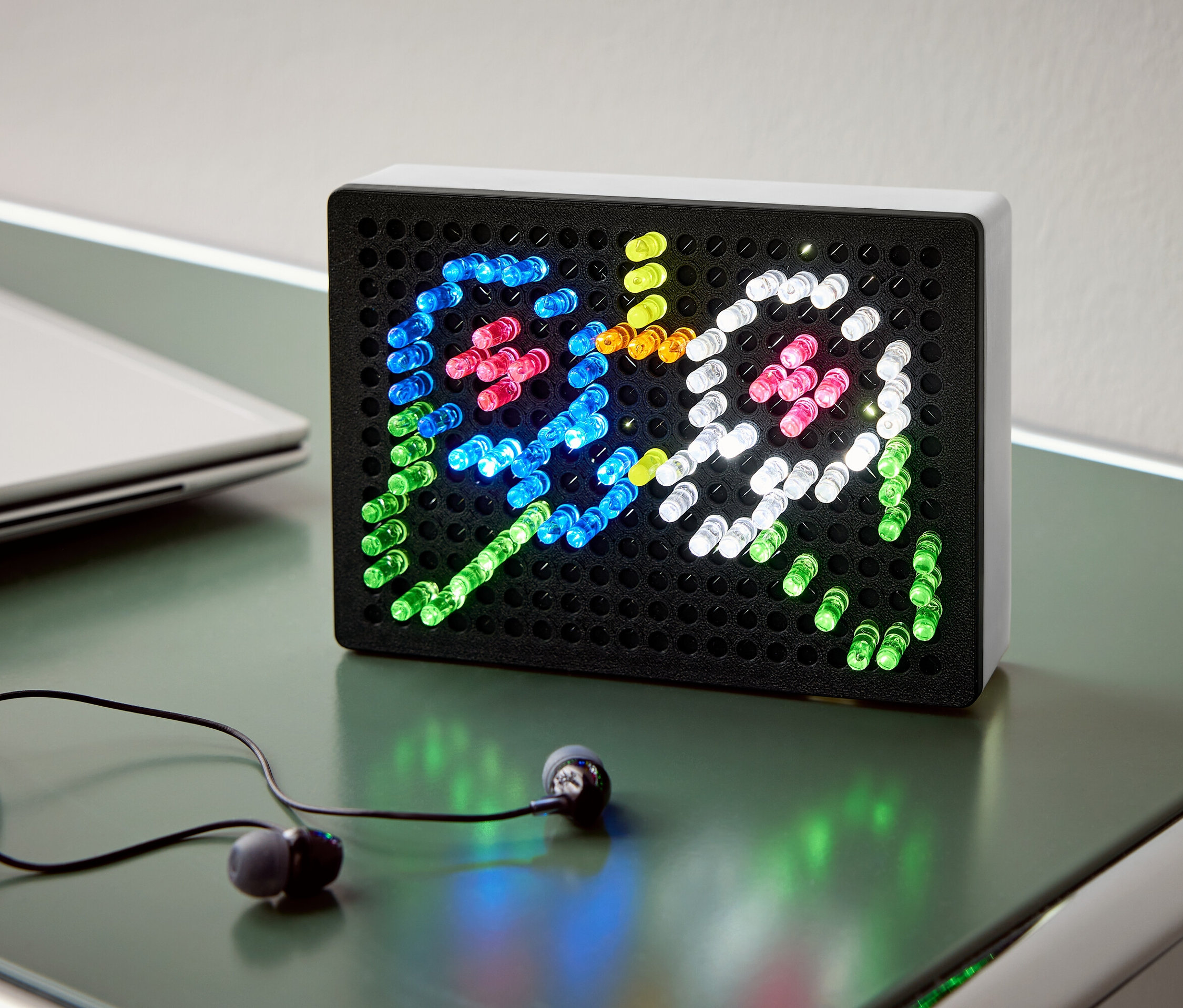 Sur une table se trouvent une boîte à lumière noire avec des lumières colorées représentant deux fantômes, ainsi que des écouteurs et un ordinateur portable.