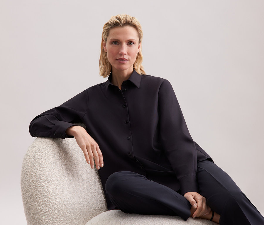 Blonde assise sur un fauteuil en chemise et pantalon noirs.