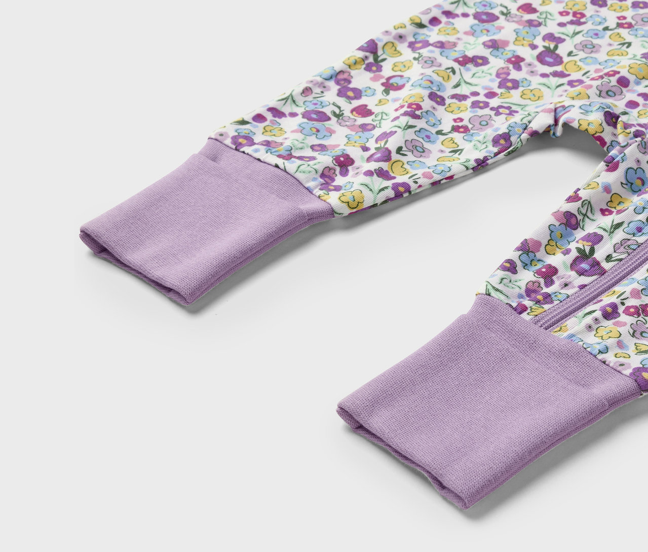 Gros plan d'une grenouillère pour bébé avec des poignets violets et un motif floral.