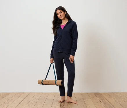 Femme tenant un tapis de yoga, portant un survêtement bleu marine et un débardeur rose.