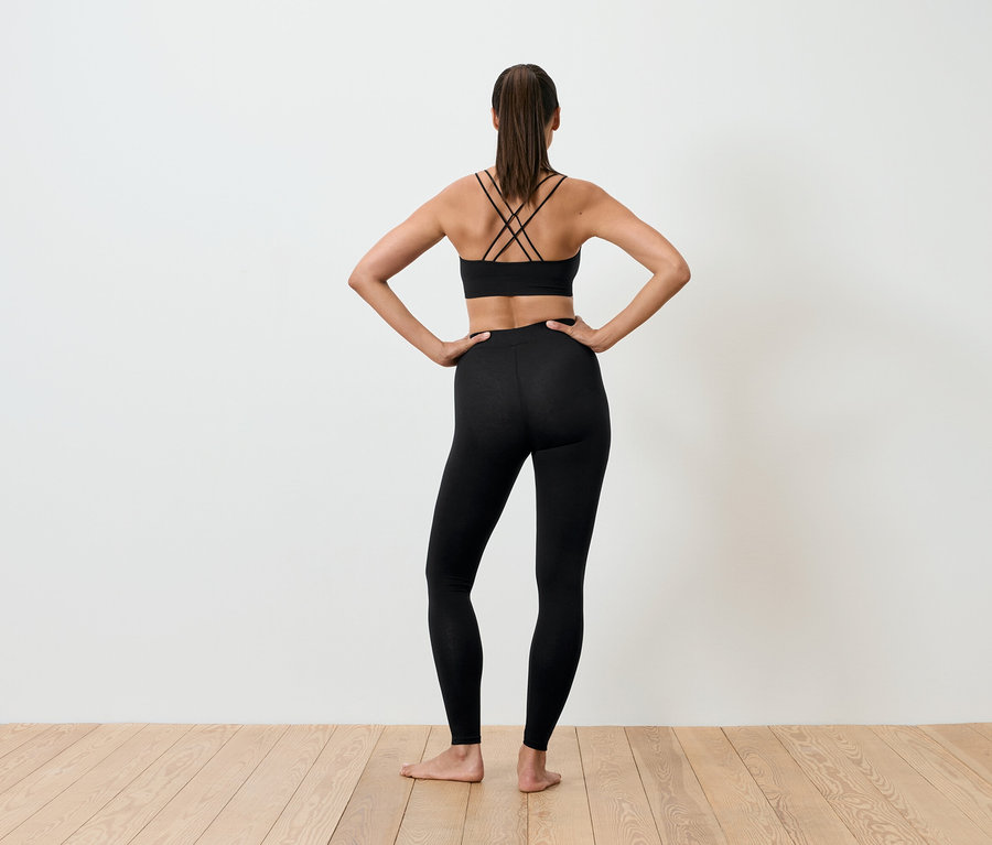 Femme dos à la caméra en soutien-gorge de sport noir et leggings, les mains sur les hanches.