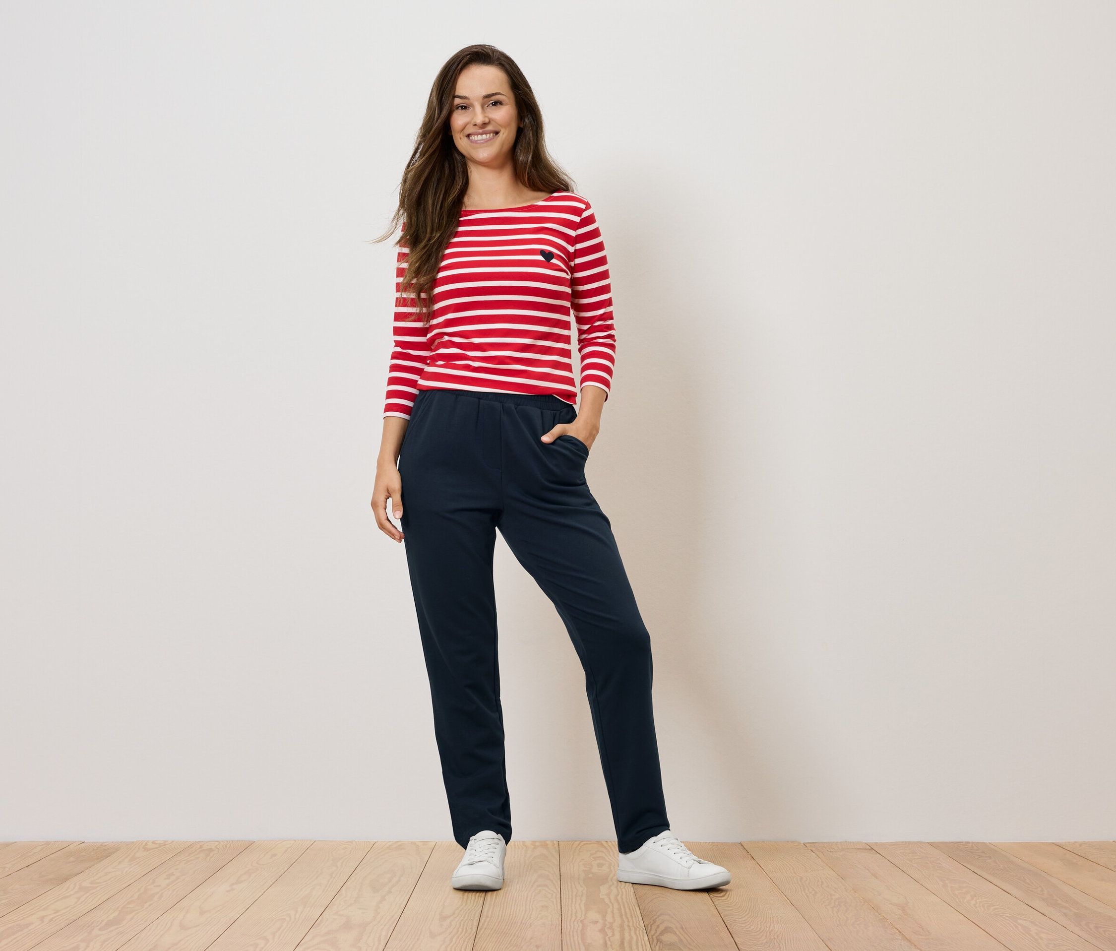 Femme debout posant dans un haut rayé rouge et blanc et un pantalon bleu marine.