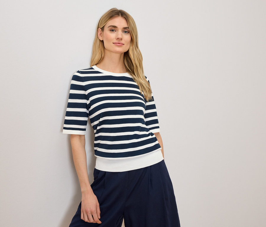 Femme blonde portant un haut rayé bleu et blanc et un pantalon bleu marine.