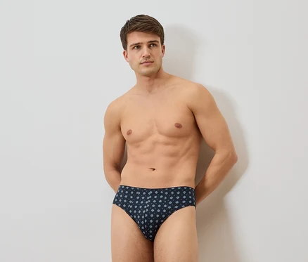 Homme torse nu portant un slip bleu marine avec un motif floral répété.