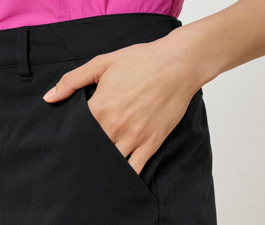 Femme avec la main dans la poche d'un pantalon noir, portant une chemise rose.