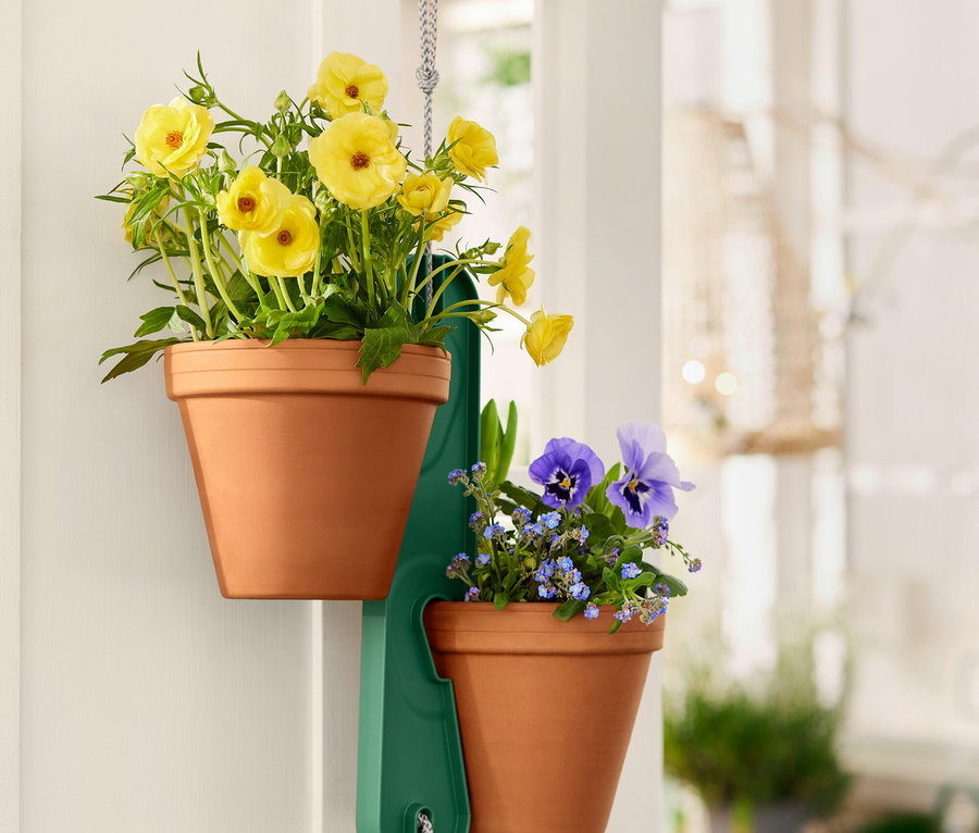 Deux pots en terre cuite avec des fleurs jaunes et bleues suspendus à un support vert sur une porte blanche.