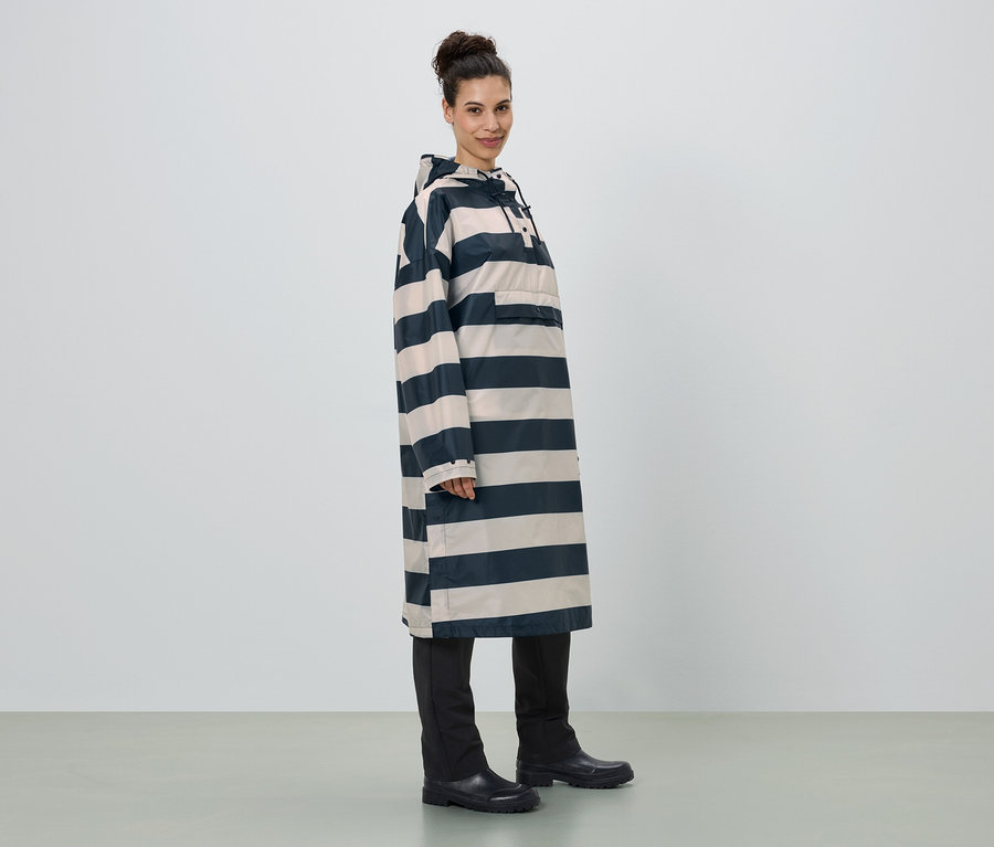 Femme debout de profil, portant un long poncho de pluie rayé avec capuche, un pantalon noir et des bottes en caoutchouc.