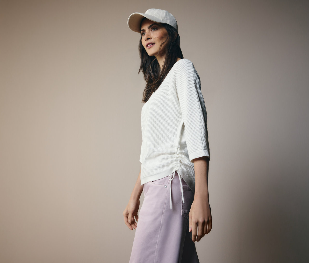 Femme portant une casquette de baseball et un pull en maille fine CECIL avec cordon de serrage sur le côté et un pantalon rose.