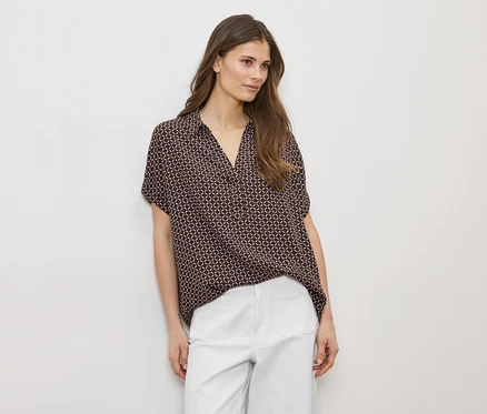 Femme portant une chemise marron à motifs et un pantalon blanc sur fond blanc.