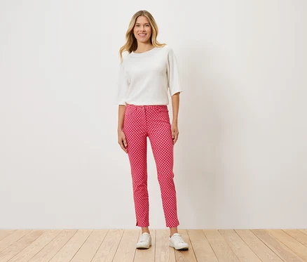 Une femme debout portant un haut blanc, un pantalon rouge à pois et des chaussures blanches.