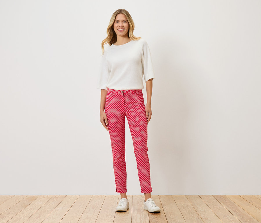 Une femme debout portant un haut blanc, un pantalon rouge à pois et des chaussures blanches.