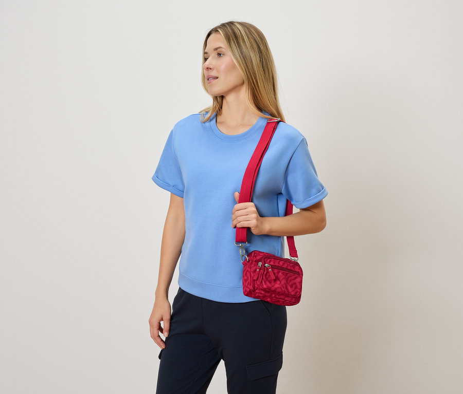 Femme portant un chemisier bleu et un pantalon bleu marine tenant un sac à bandoulière rouge.