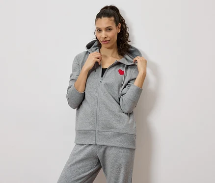 Femme portant un survêtement gris avec un cœur rouge sur la veste.