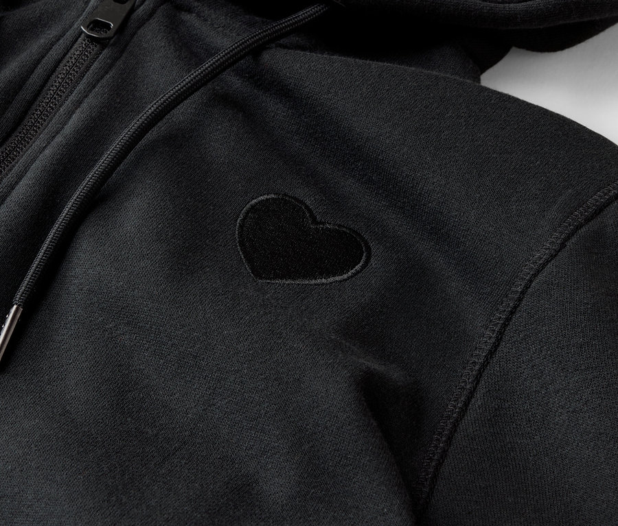 Gros plan sur un sweat à capuche noir zippé avec une petite application en forme de cœur.
