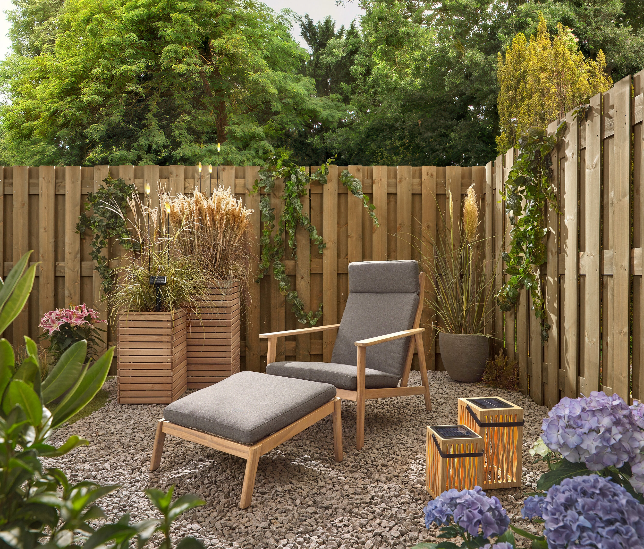 Un jardin avec une chaise et un tabouret gris, deux lanternes solaires en bambou et 5 piquets à LED solaires.