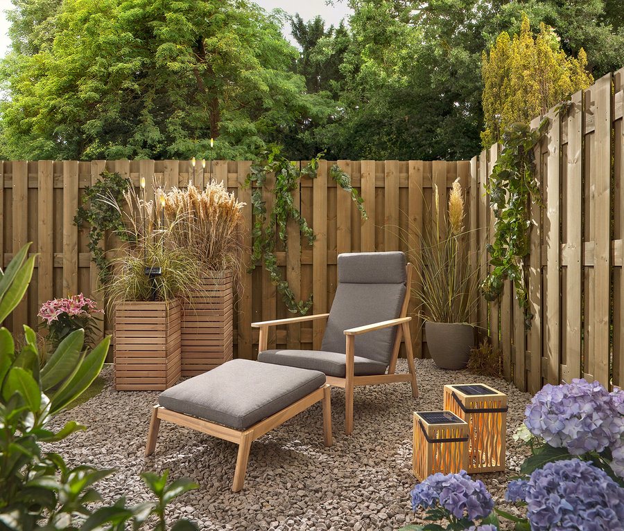 Un jardin avec une chaise et un tabouret gris, deux lanternes solaires en bambou et 5 piquets à LED solaires.