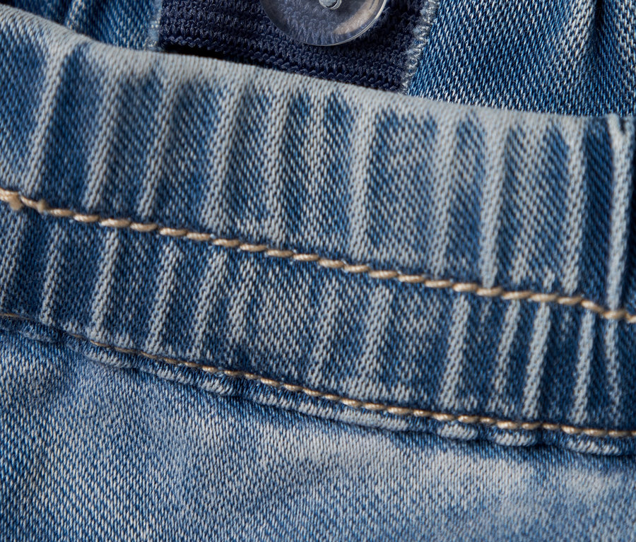 Gros plan d'un jean bleu clair avec une taille élastique réglable et un bouton transparent.