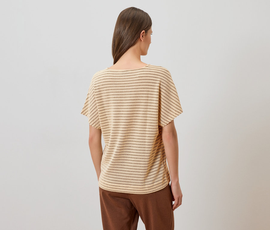 Vue arrière d'une femme aux longs cheveux bruns portant un haut beige à pois et un pantalon marron sur un fond blanc.