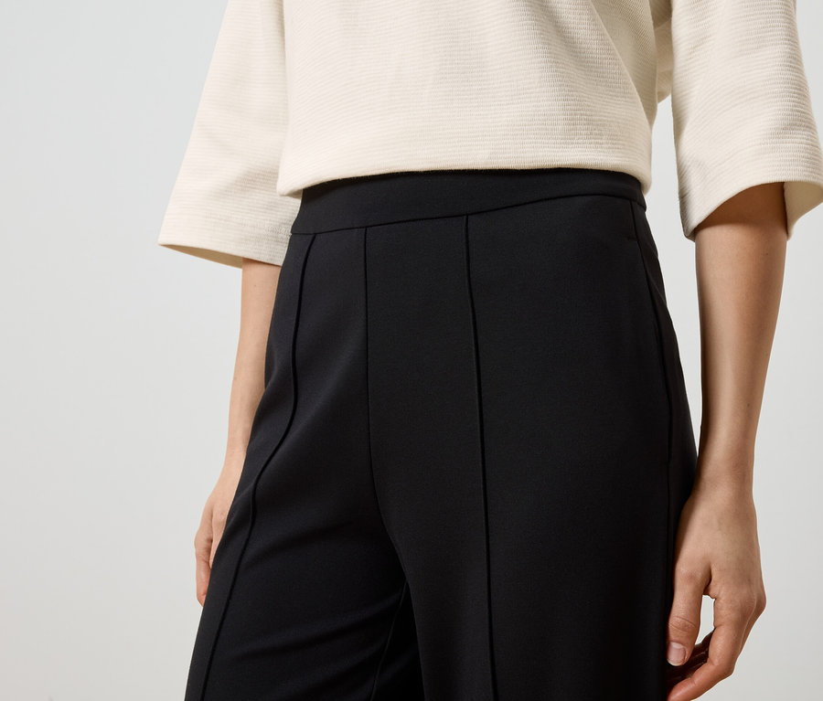 Gros plan d'une femme portant un haut beige et un pantalon noir à plis.
