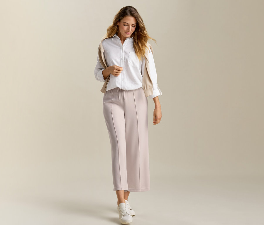 Femme portant une blouse longue en lin blanche et un pantalon en mélange de modal sable. Un cardigan beige est sur ses épaules.