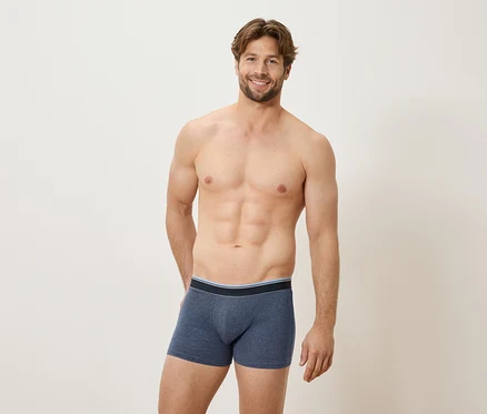 Homme torse nu souriant portant un caleçon boxer bleu.