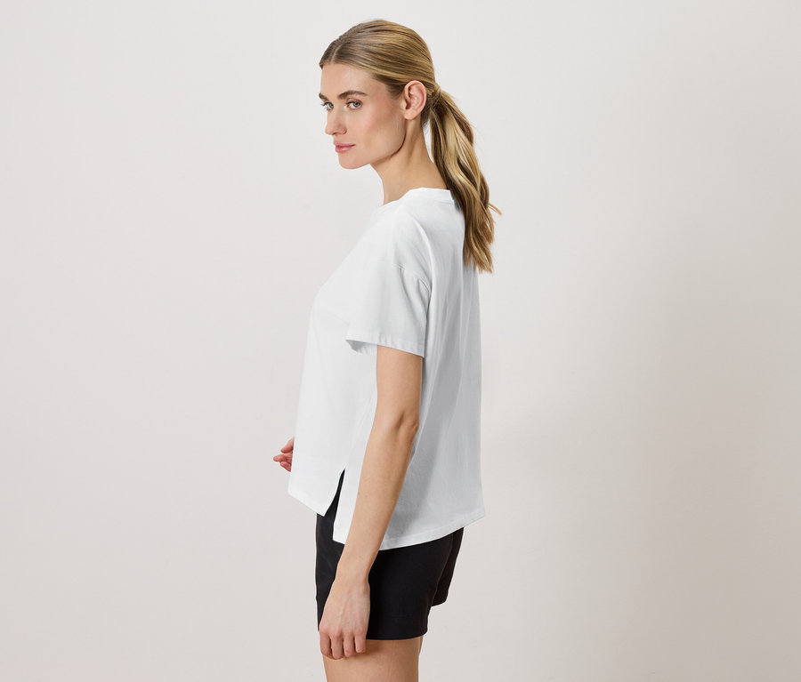 Femme blonde portant un t-shirt blanc et un short noir, vue latérale.