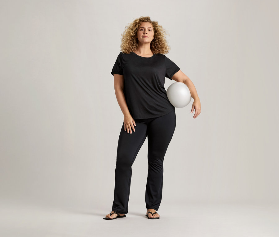 Femme aux cheveux bouclés, t-shirt noir et pantalon noir tenant un ballon blanc.