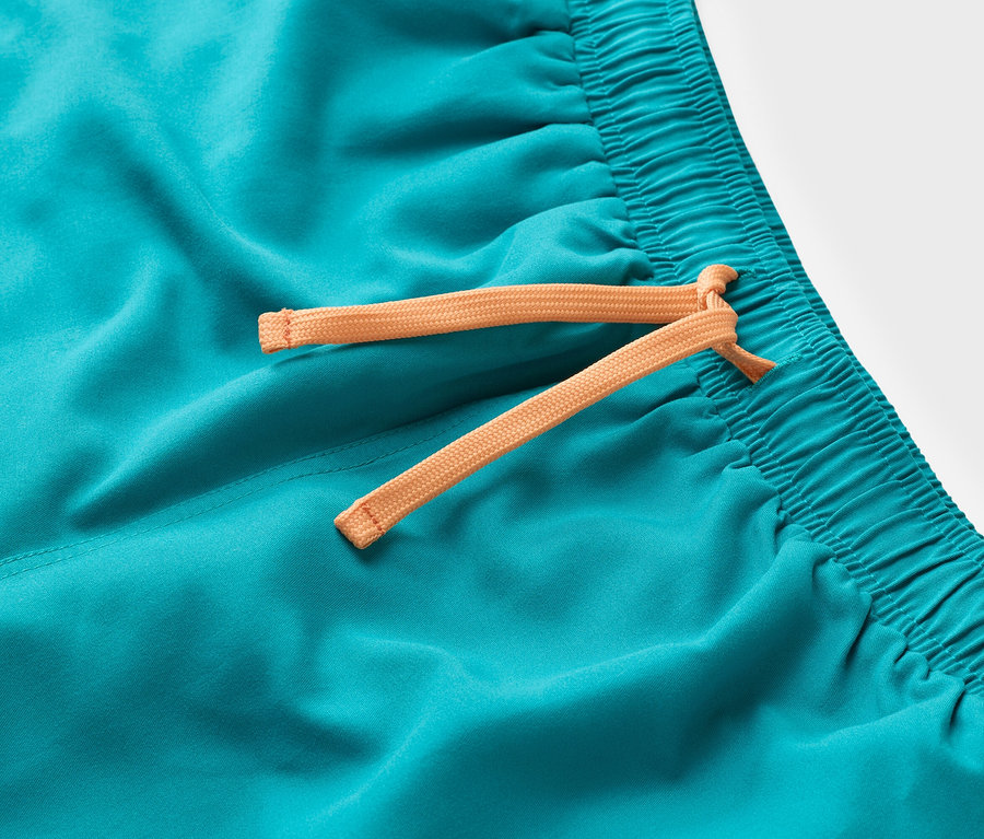 Gros plan d'un short de bain turquoise avec un cordon de serrage orange.