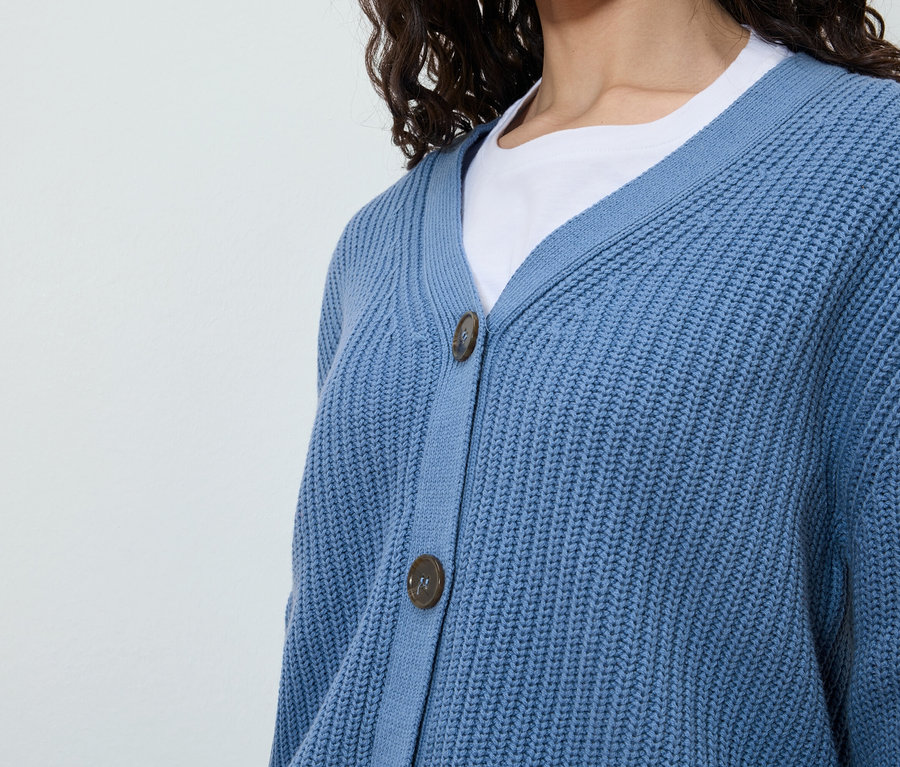 Une femme porte un cardigan bleu sur un t-shirt blanc.