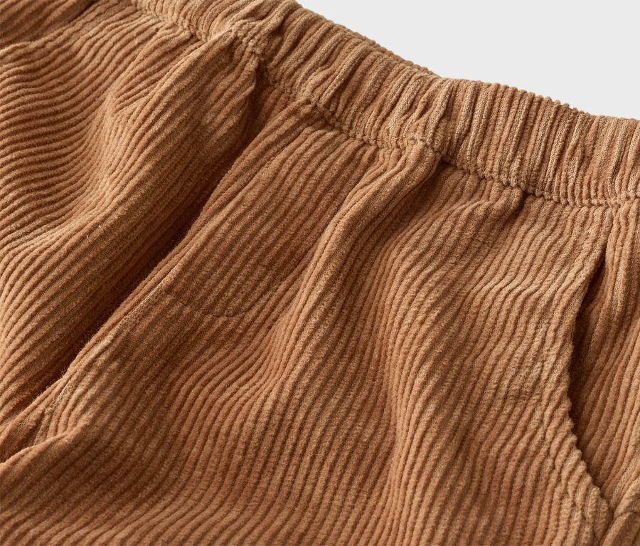 Gros plan d'un pantalon en velours côtelé marron clair avec une taille élastique et une poche latérale.