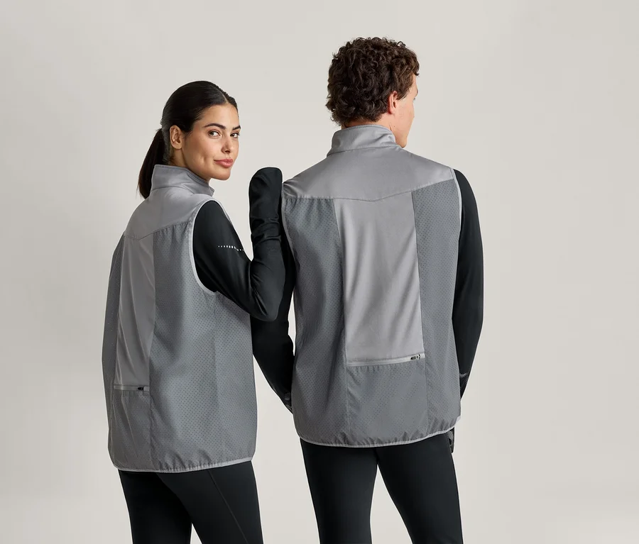 Une femme regarde par-dessus son épaule, tous deux portant des gilets gris sur des vêtements noirs.