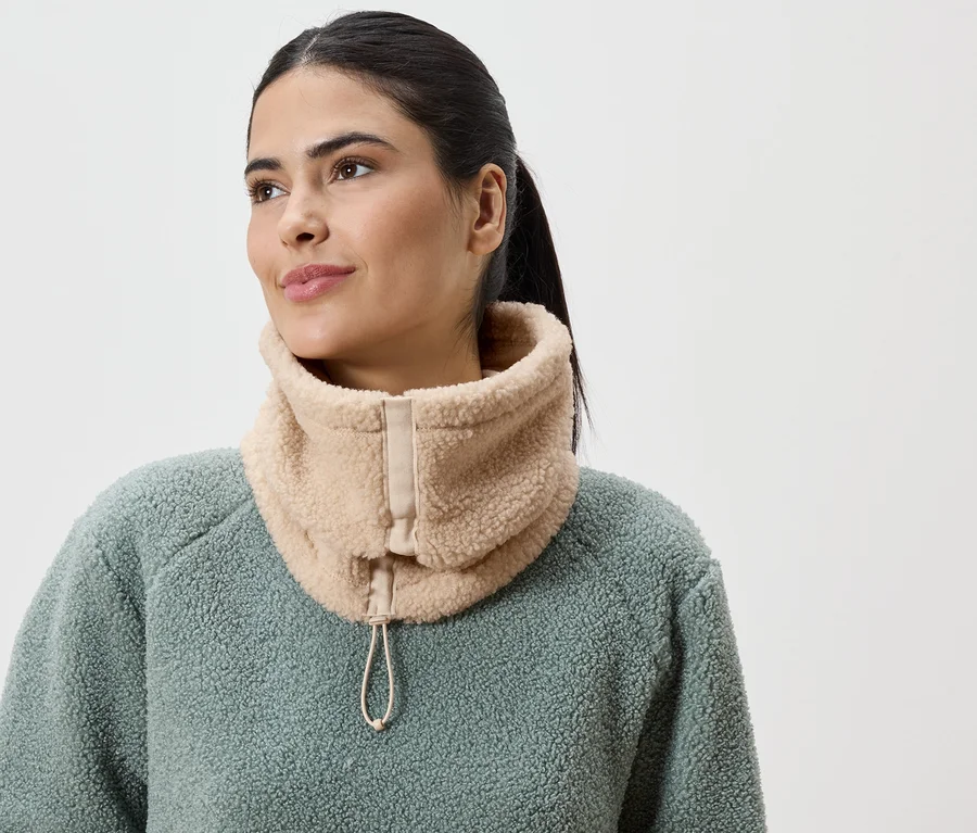 Femme portant un snood en peluche beige avec cordon de serrage sur un haut en polaire vert.