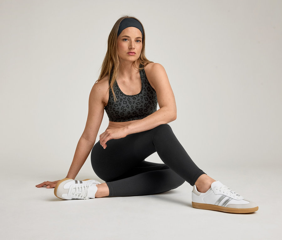 Femme assise portant un soutien-gorge de sport, un bandeau et un legging de sport « ActiveSoft ». Elle porte des baskets blanches.