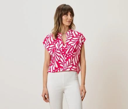 Femme portant un chemisier rose à motif de feuilles blanches et un pantalon blanc.