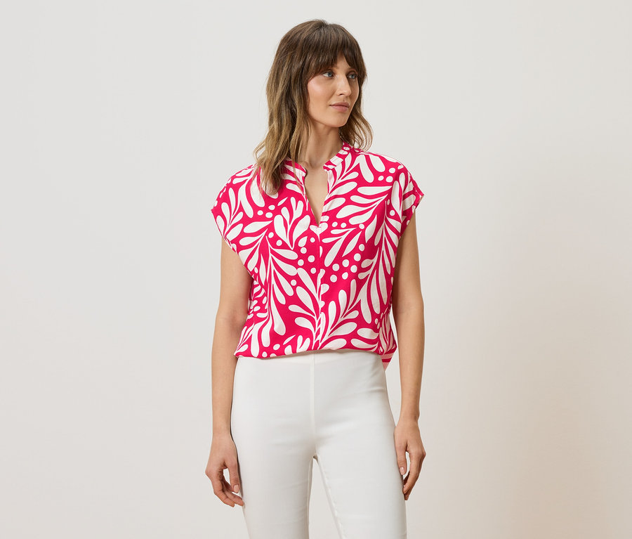 Femme portant un chemisier rose à motif de feuilles blanches et un pantalon blanc.