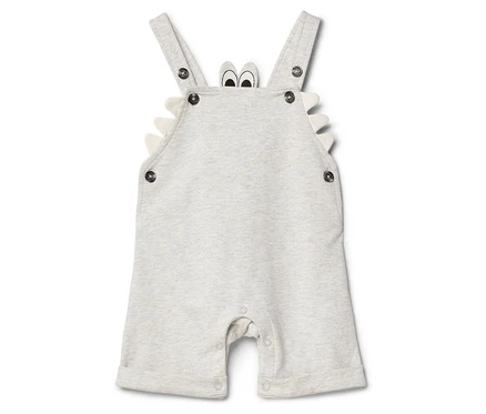 Salopette de bébé claire avec bretelles, boutons et motif crocodile.