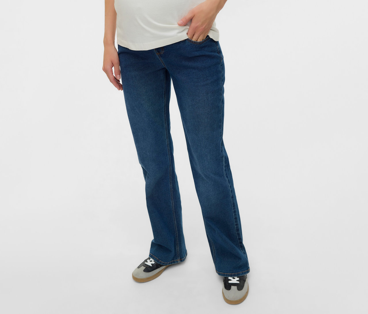 Femme enceinte portant un jean évasé MAMALICIOUS «
MLEDINA
» et un t-shirt blanc, main dans la poche.