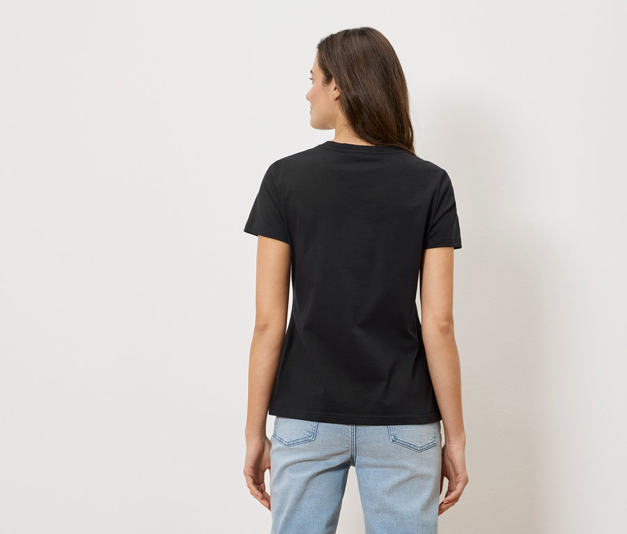 Vue arrière d'une femme aux longs cheveux bruns portant un t-shirt noir et un jean bleu clair.