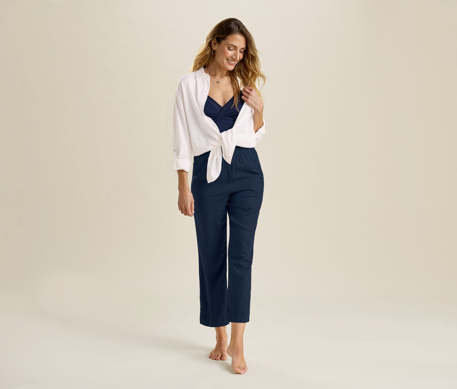 Femme portant un pantalon en lin bleu marine et une blouse longue en lin blanche nouée sur le devant.