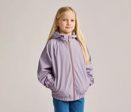 Une fille blonde, en jean et veste à capuche violette, les mains dans les poches.