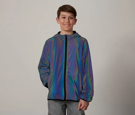 Un adolescent souriant aux cheveux bruns porte une veste irisée à capuche et à fermeture éclair sur un jean gris.