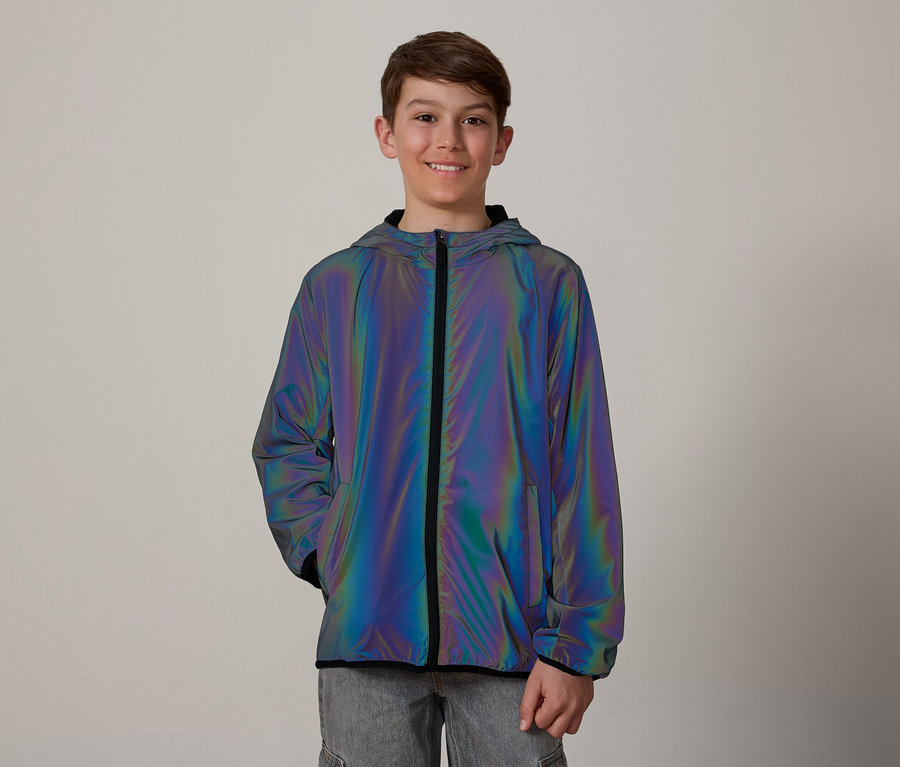 Un adolescent souriant aux cheveux bruns porte une veste irisée à capuche et à fermeture éclair sur un jean gris.