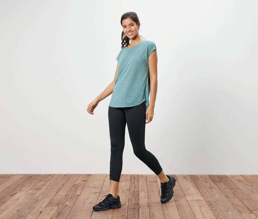 Une femme marche avec un t-shirt turquoise, un legging noir et des chaussures de course noires.