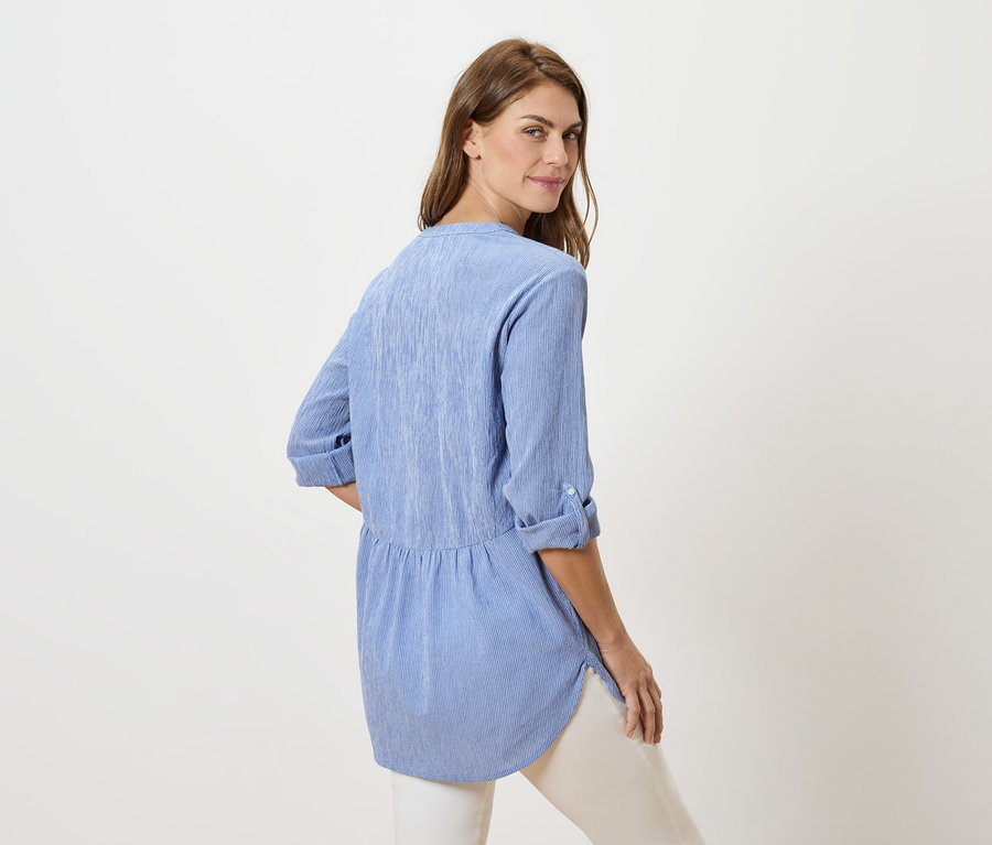 Une femme regarde par-dessus son épaule, portant un chemisier bleu et un pantalon blanc.