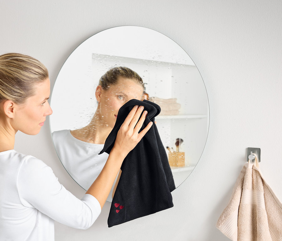 Une femme nettoie un miroir rond embué avec un chiffon noir.