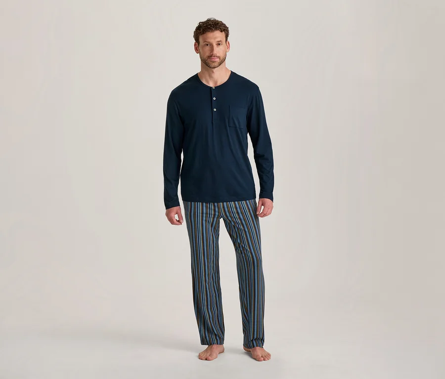 Homme debout pieds nus, portant un haut de pyjama bleu marine à manches longues avec des boutons et une poche, et un pantalon de pyjama rayé bleu, marron et noir.
