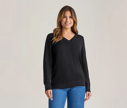 Femme souriante aux longs cheveux bruns, portant un pull noir à col en V et un jean bleu.